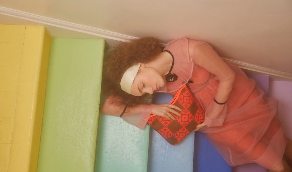 Model lying on stairs holding a Cross Carry Crossbody in Lattice Flower Tile Conker print